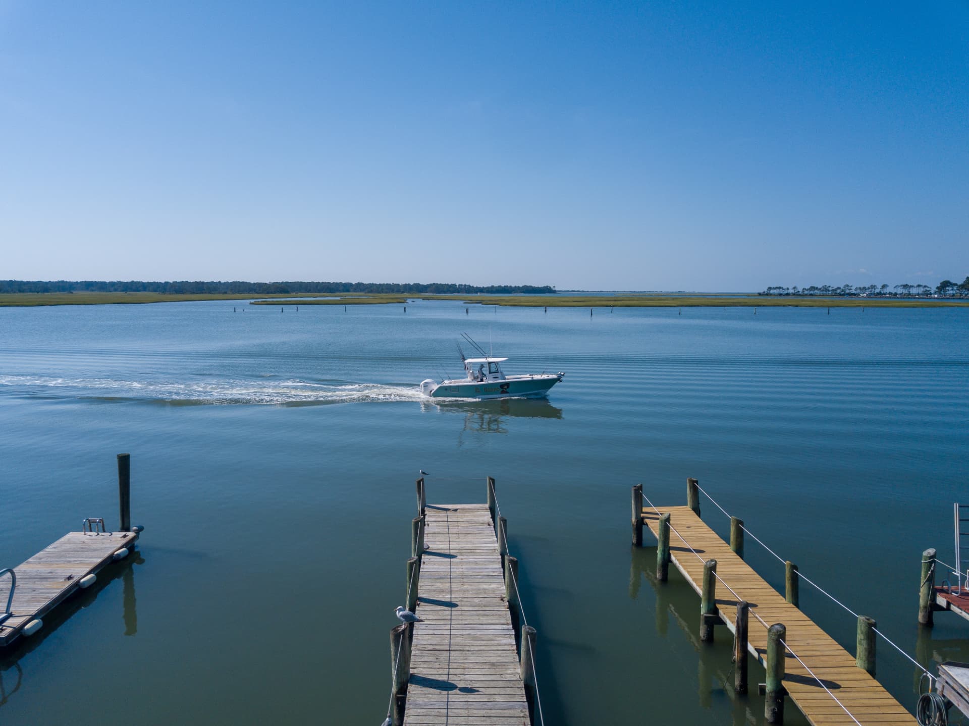 Boat cruising on the calm channel past wooden docks at Channel Landing
